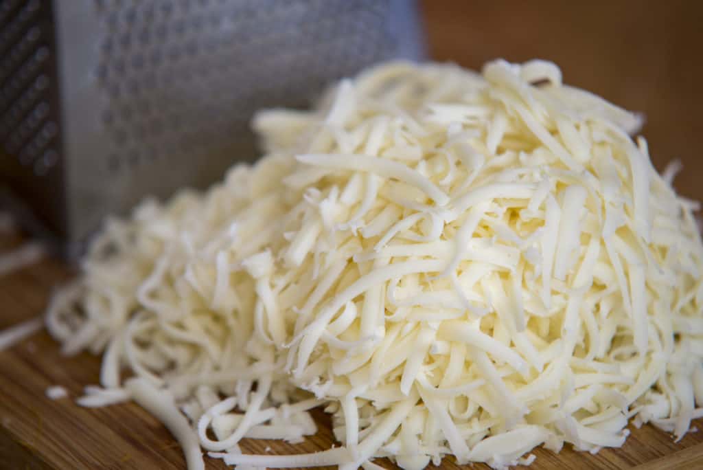Mozzarella-Käse auf einem Schneidebrett mit einer Reibe zerkleinern